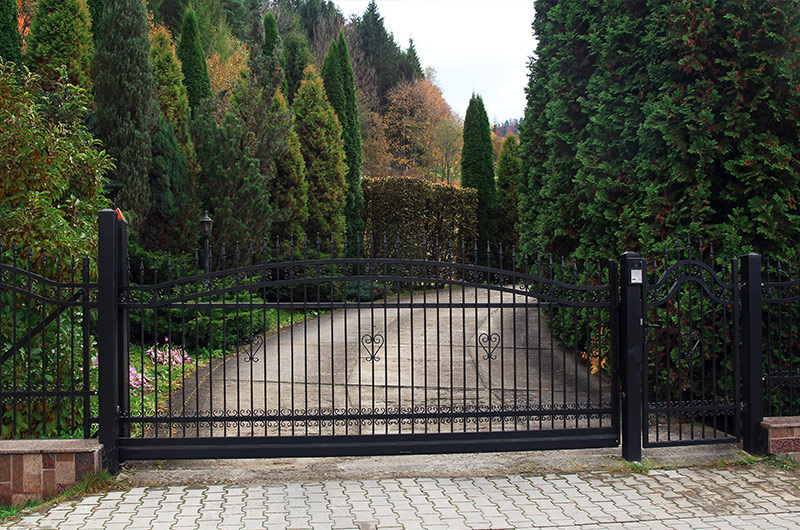 Iron gate at farm & ranch entrance with tall cypress trees . rural farm gate total property wireless access with CellGate
